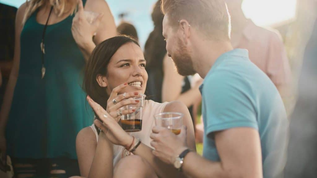 A woman and man smiling and talking while holding drinks at a social gathering.