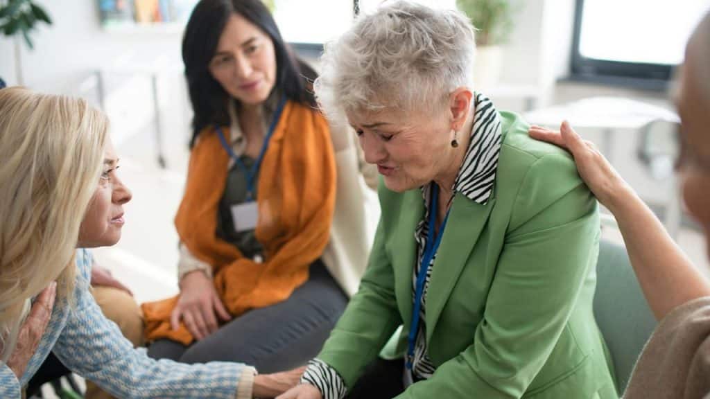 A group of senior people sitting in a circle during a therapy session consoling a depressed woman.