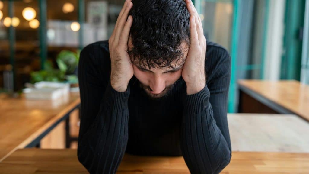 A man sits at a table holding his head in stress.