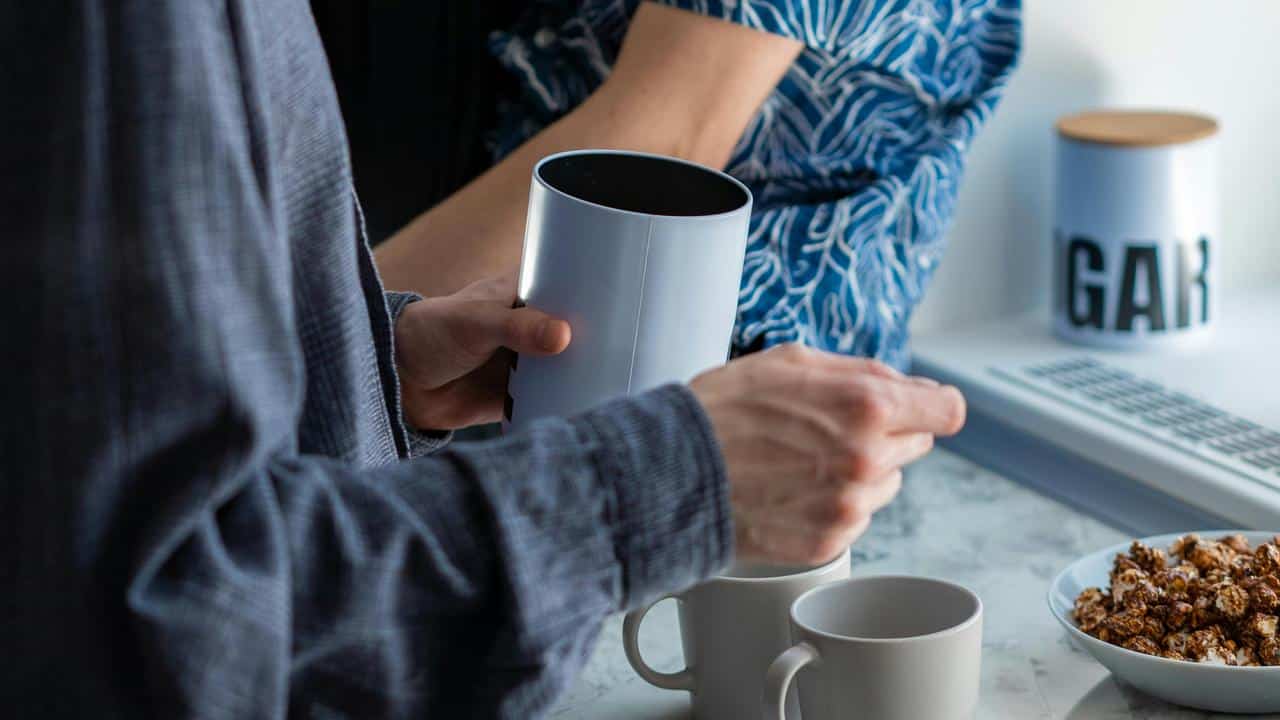 A person preparing coffee in a kitchen beside another person.