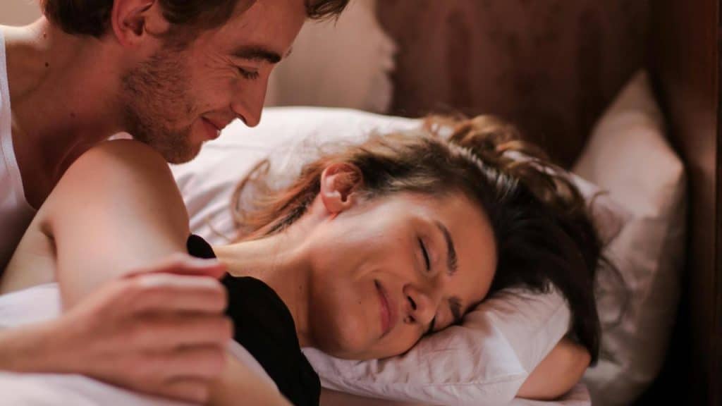 A couple lying in bed, smiling and sharing a tender moment.
