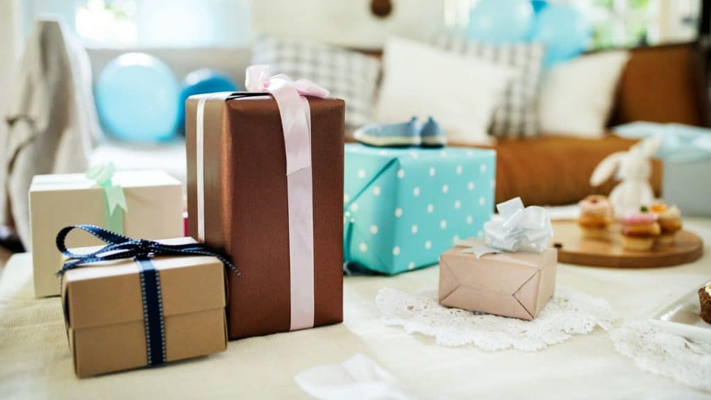 Wrapped gift boxes with ribbons sit on a table next to cupcakes and blue balloons.