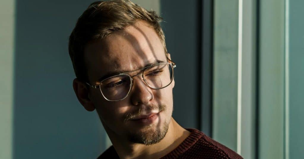 A man wearing glasses looking thoughtfully to the side in sunlight.