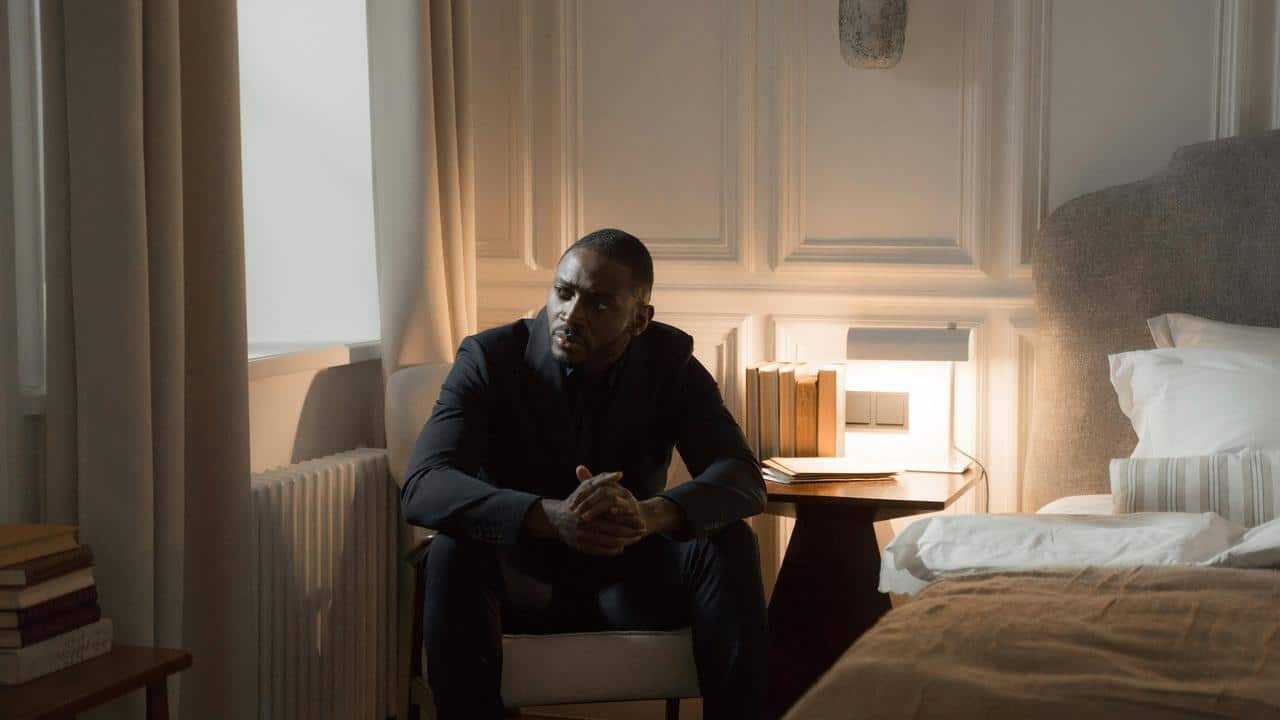 A man in a suit sitting on a chair in a dimly lit bedroom.