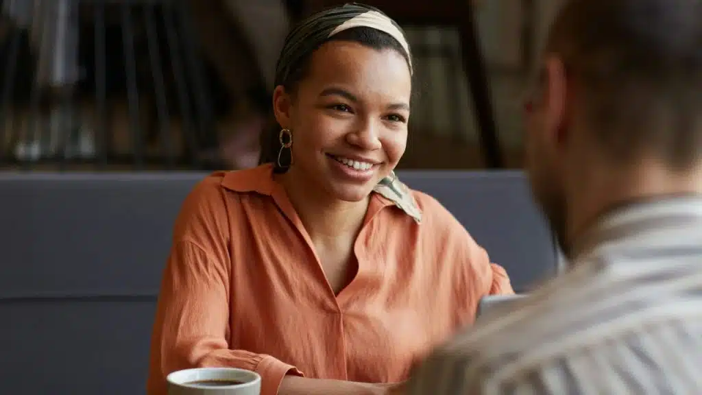 A woman with a striped headband smiling warmly at a man in a cafe setting.
