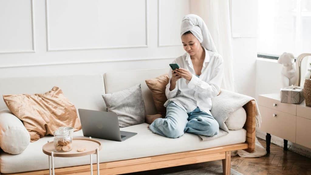 A woman with a towel on her head sitting on a couch and using her phone.