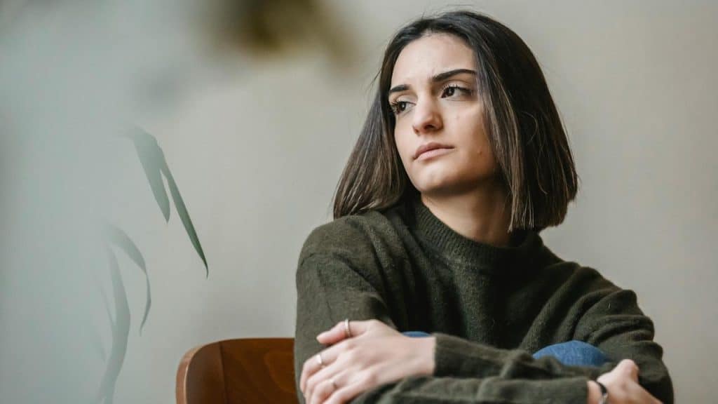 A woman sitting with folded arms and looking away thoughtfully.