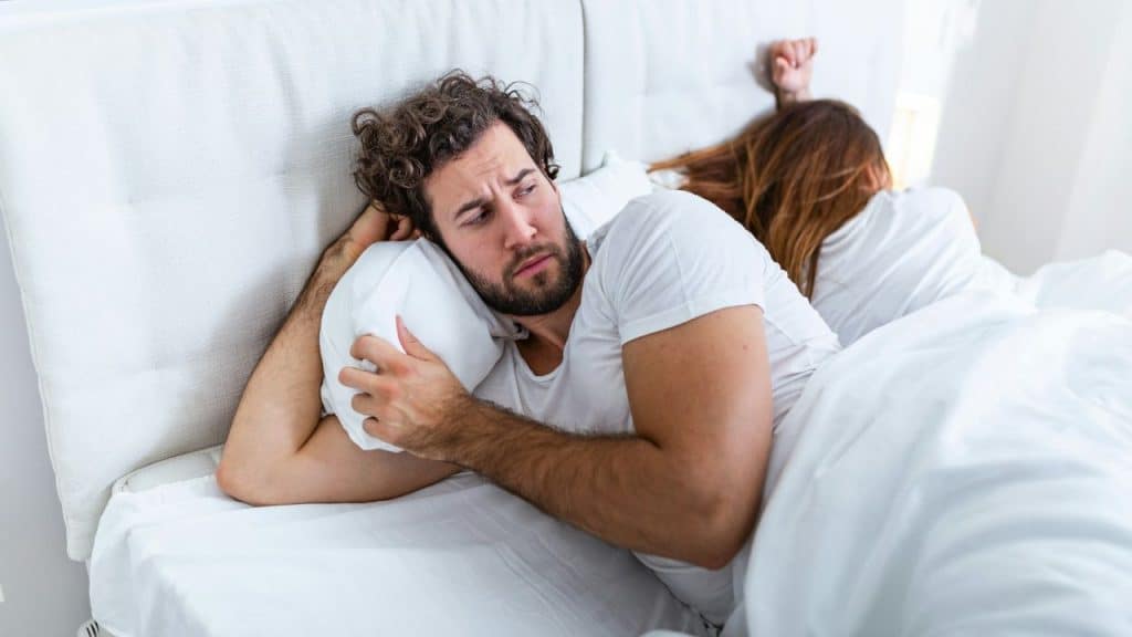 A man lies in bed looking away while a woman lies with her back turned to him.