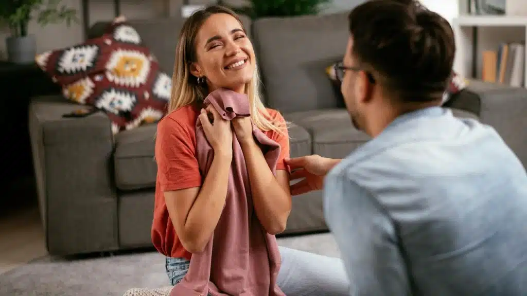 A woman smiling while holding a scarf as she talks with a partner on the floor.