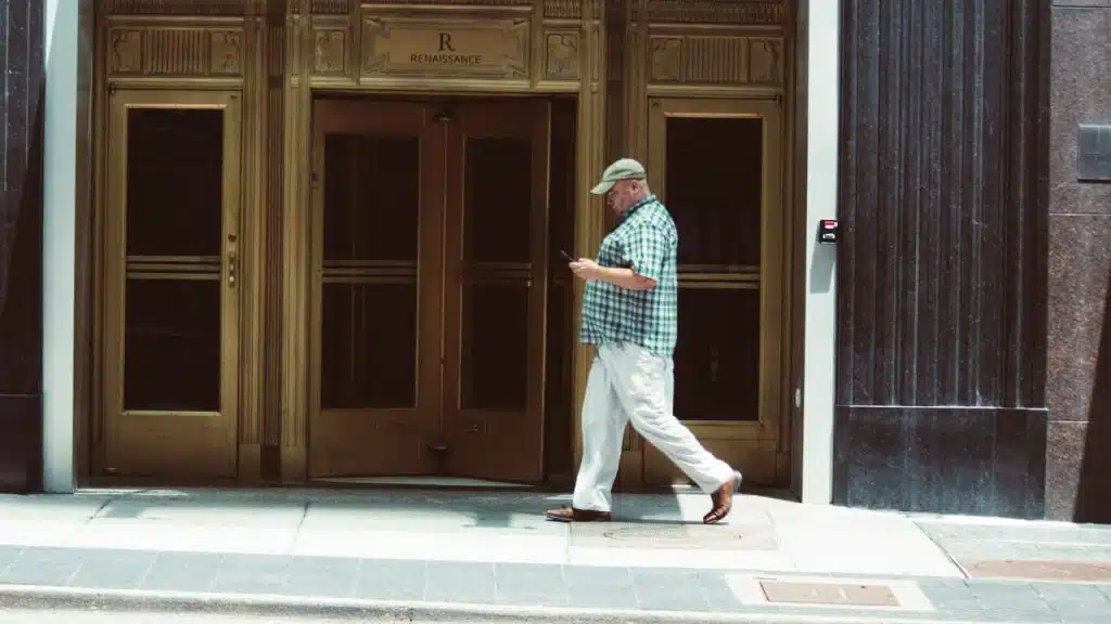 A man in a plaid shirt and cap walks past large gold-framed glass doors.