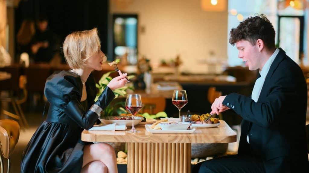 A man and woman in formal attire eat a meal at a restaurant table.
