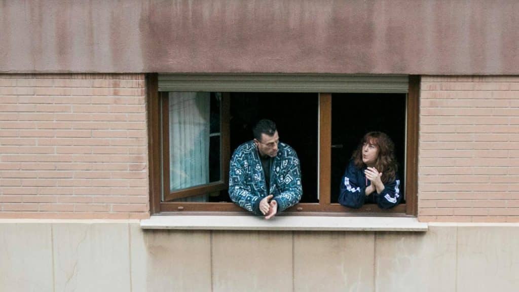 A man and a woman standing at the window of their house.