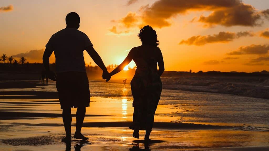 Silhouette of a couple holding hands and walking on the beach.