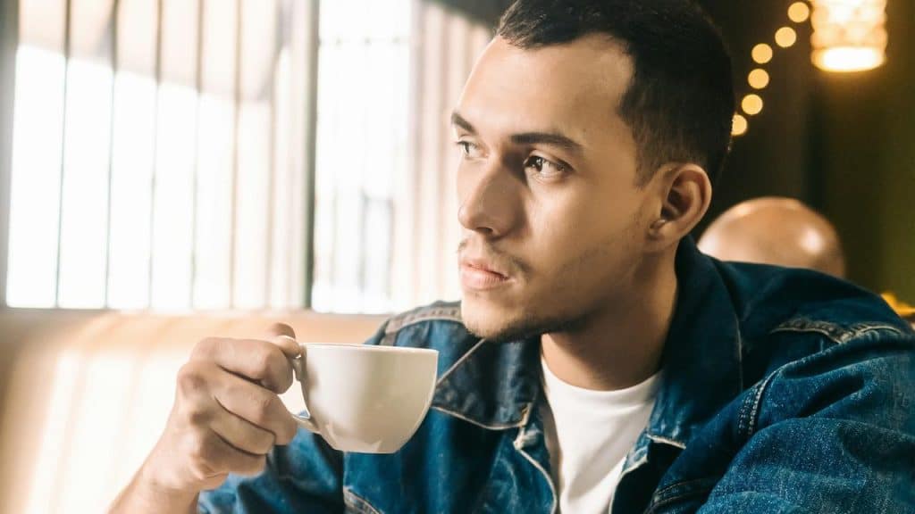 A man in a denim jacket holds a cup of coffee.