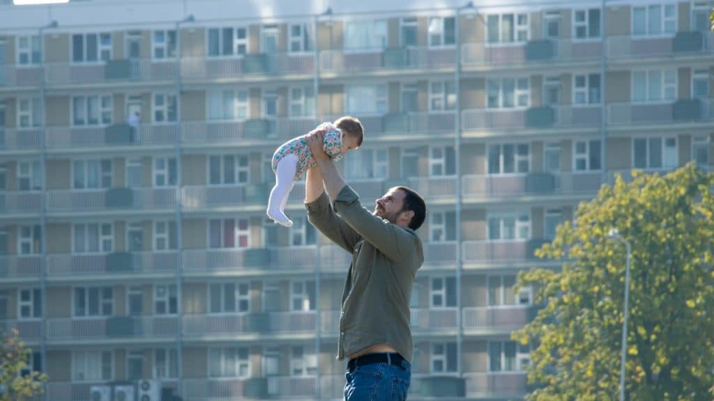 A man outdoors holds a small baby high up in the air toward the sky.