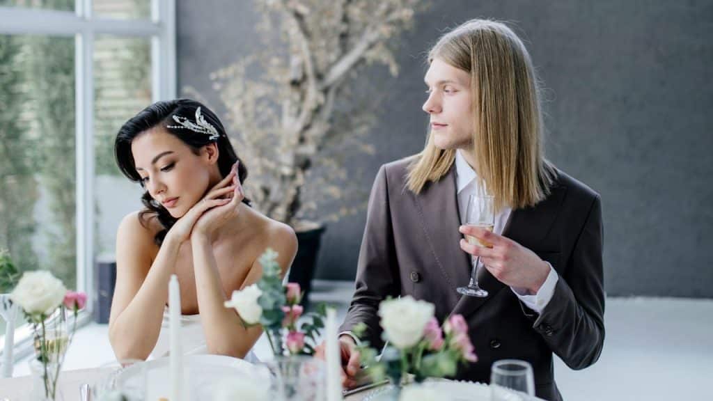A person with long hair looks away while a seated woman rests her head on hands.