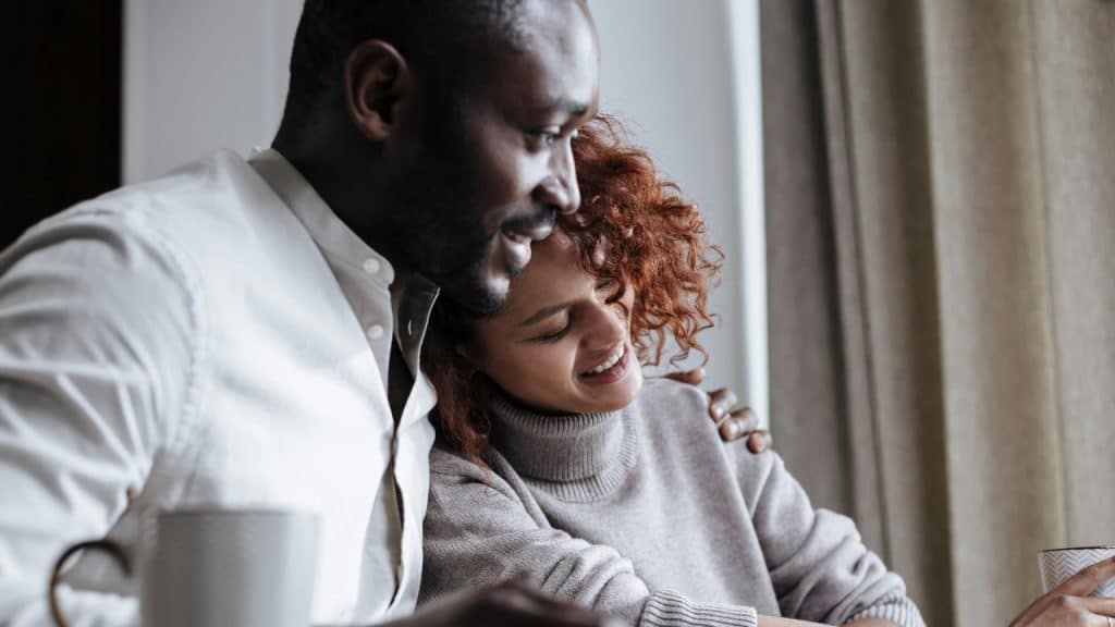 A man with his arm around a woman looks down at something out of frame.
