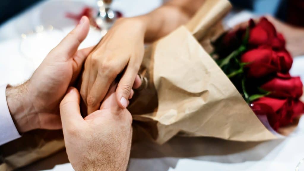 A couple holding hands with a bouquet of roses.