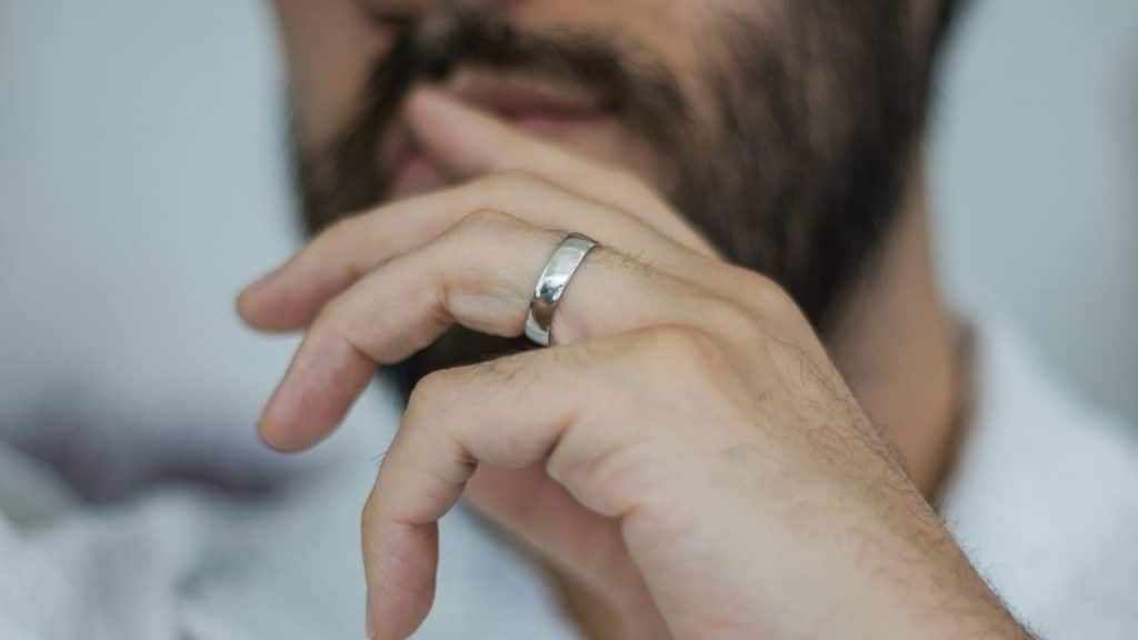 A close-up shows a man's hand with a silver band on his ring finger.