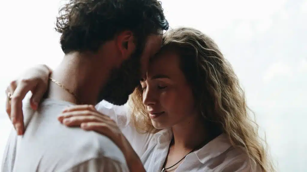 A man and woman stand close together with their foreheads touching and eyes closed.