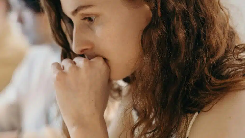 A woman with curly hair resting her fist against her mouth while looking thoughtful.