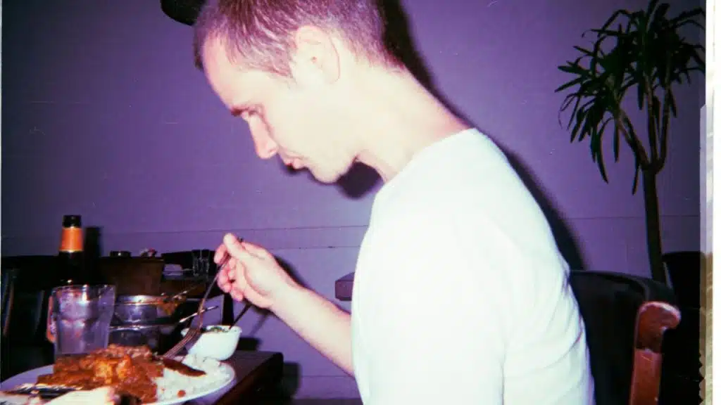 A man in a white shirt eating a meal at a table with a purple tint.