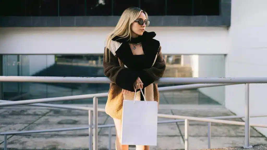 A fashionable woman wearing shades and carrying a shopping bag.