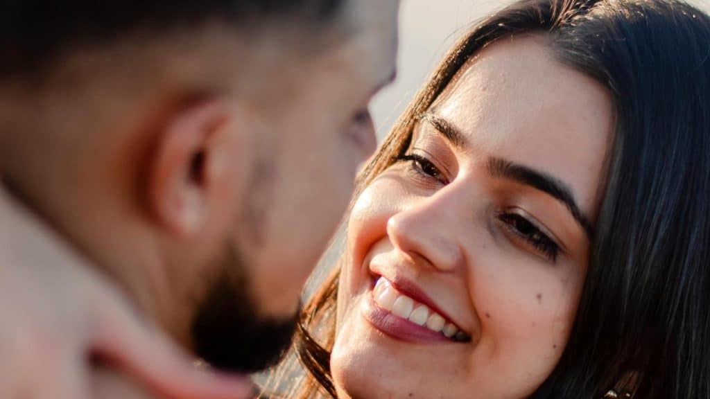A woman smiling warmly at a man in a close-up outdoor shot.