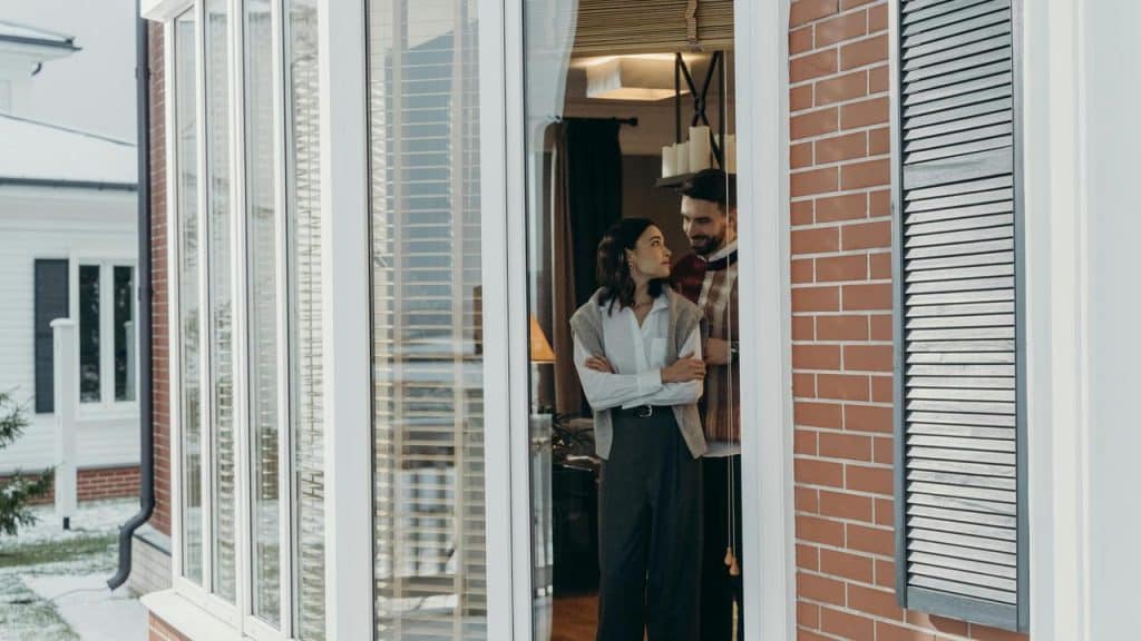 A couple standing together by a window, looking at each other affectionately.