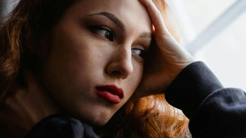 A close-up of a woman looking worried with her hand on her forehead.
