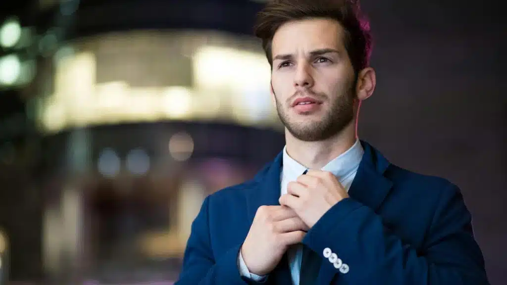 A man in a suit adjusting his tie and looking worried.