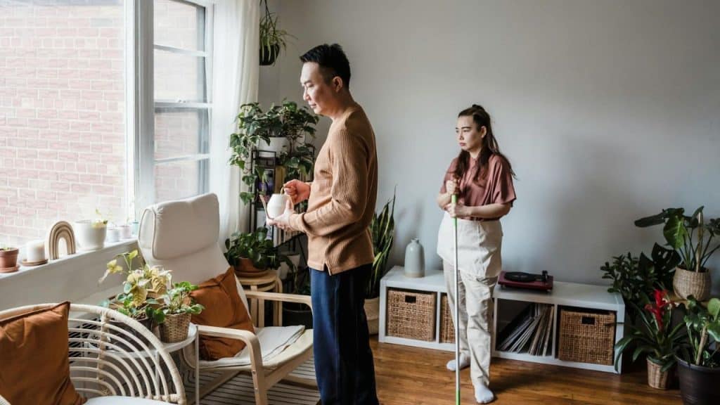 A man holds a small kettle while a woman stands nearby holding a mop handle.