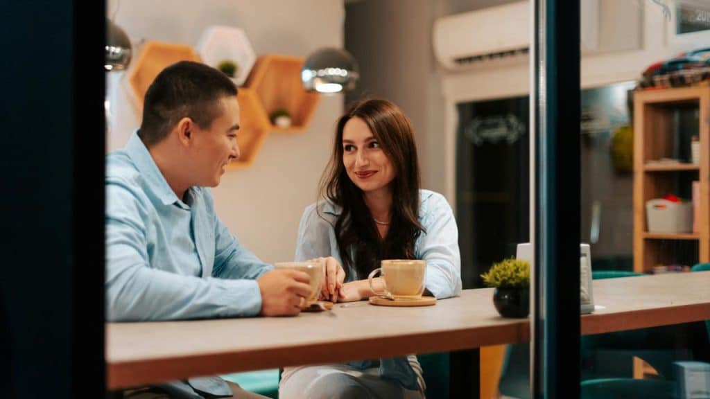 A couple sits at a café counter, smiling and talking over coffee.