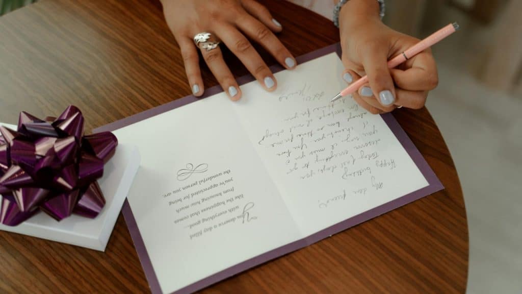 A person with light blue nail polish writes in a card on a wooden table.