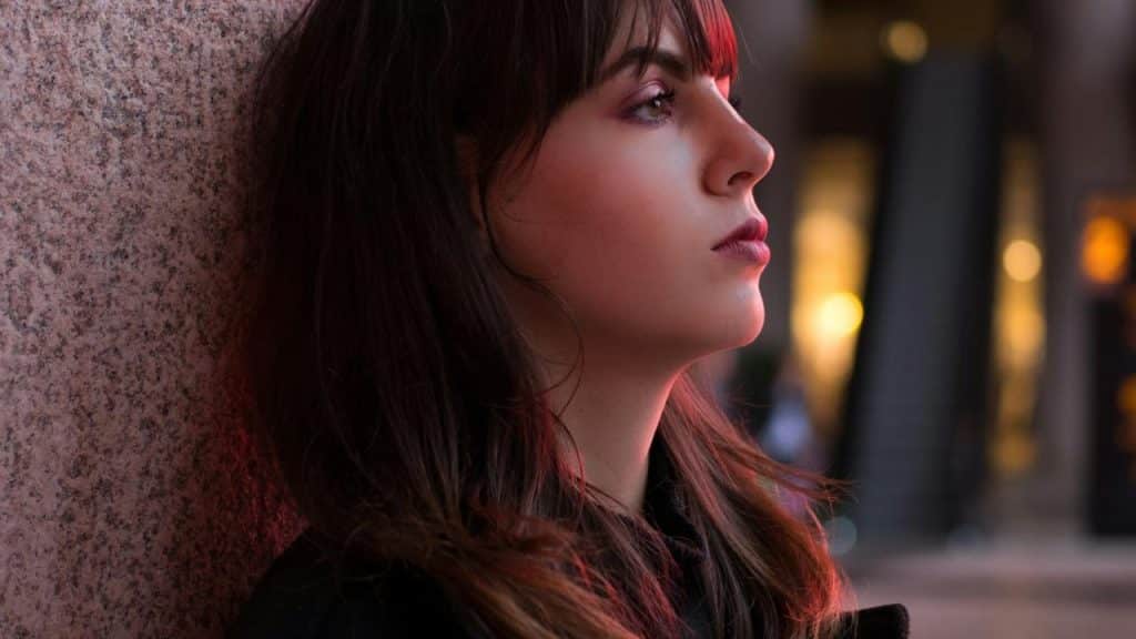 A woman with bangs gazing sideways under soft city lights.