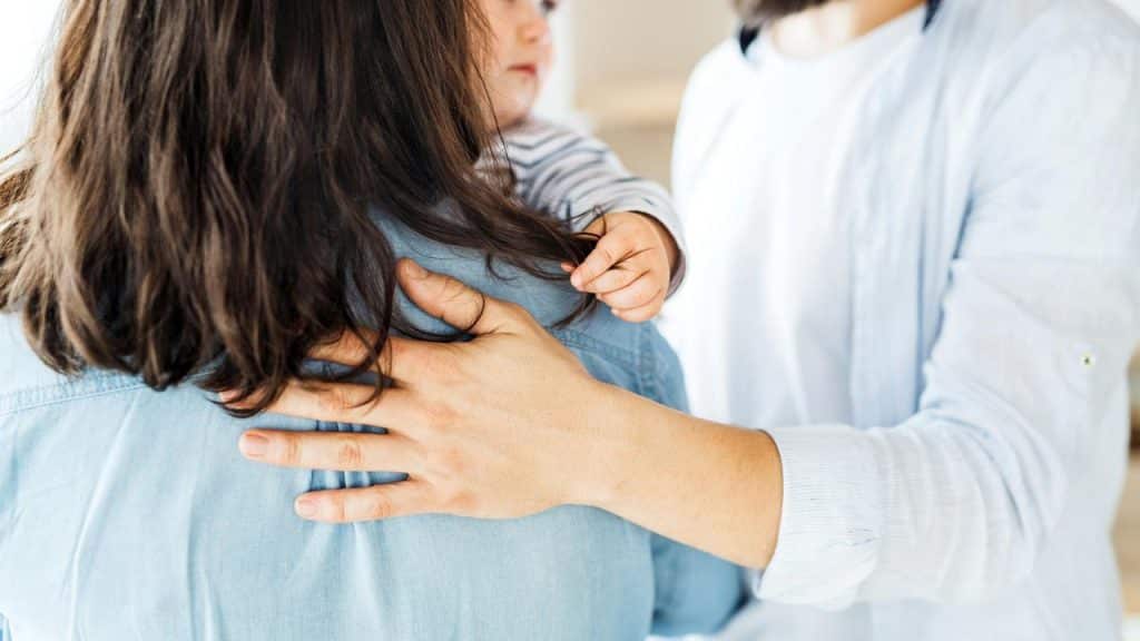 A parent holding a child while offering comfort from behind.