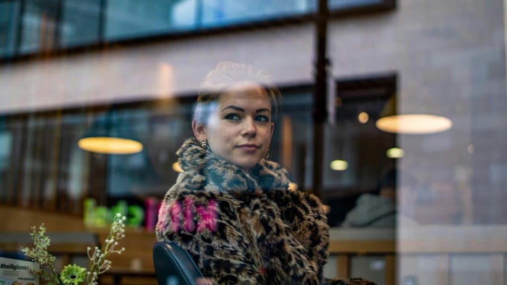 A woman in a fur coat sitting by a window and looking outside.
