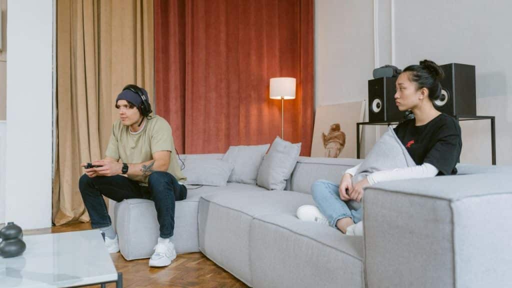 A man wearing a headset plays video games while a woman sits nearby looking away.