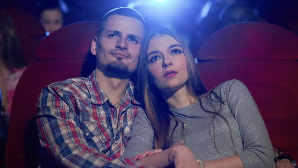 A man and woman lean against red theater seats, looking upward toward a blue light.