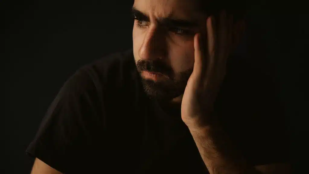 A close-up of a man with a beard resting his head on his hand indoors.