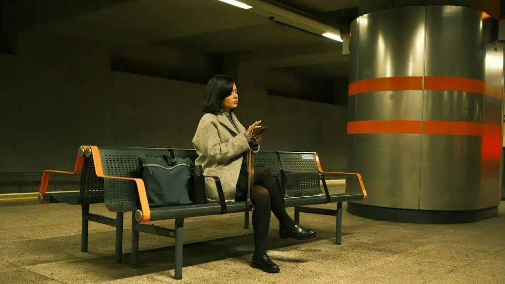 A woman using her phone sits on a bench in a subway.
