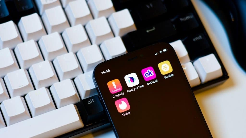 A cell phone with multiple apps on its screen placed next to a keyboard.