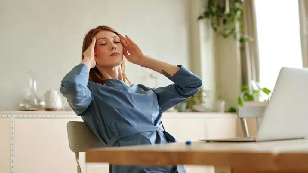 A woman sitting at a desk with a laptop and holding her head in stress.