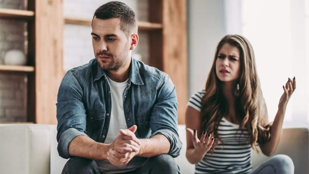 A man and a woman are having a quarrel while sitting on a sofa together.