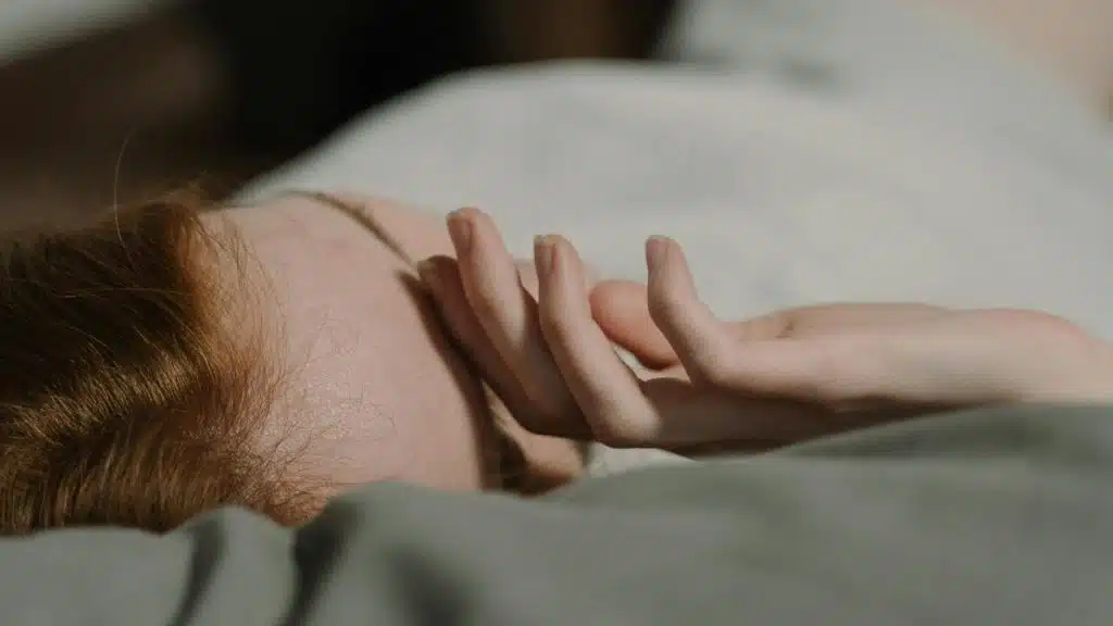 A person lying down with their hand resting gently on the bed.