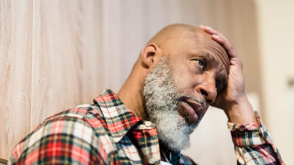 An older man in a plaid shirt resting his head on his hand.