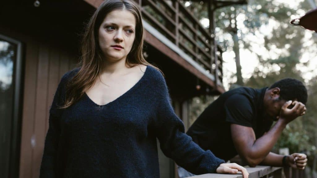 A woman with smudged makeup stands in front of a man leaning on a wooden railing.