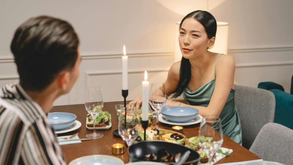 A woman in a green dress sits at a candlelit dinner table talking to a man.