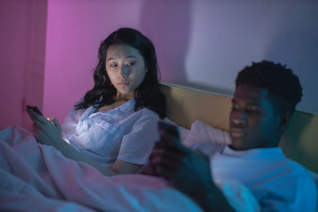 Couple in bed on phones ignoring each other