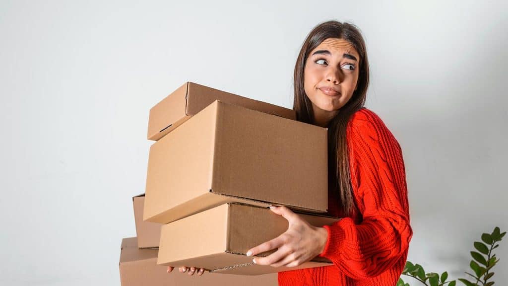 A woman in a red sweater holds several stacked cardboard boxes.